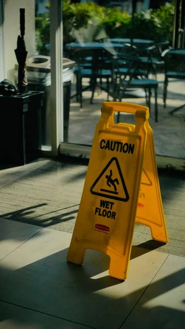 Person in protective gear cleaning a floor with disinfectant spray and cloth indoors.